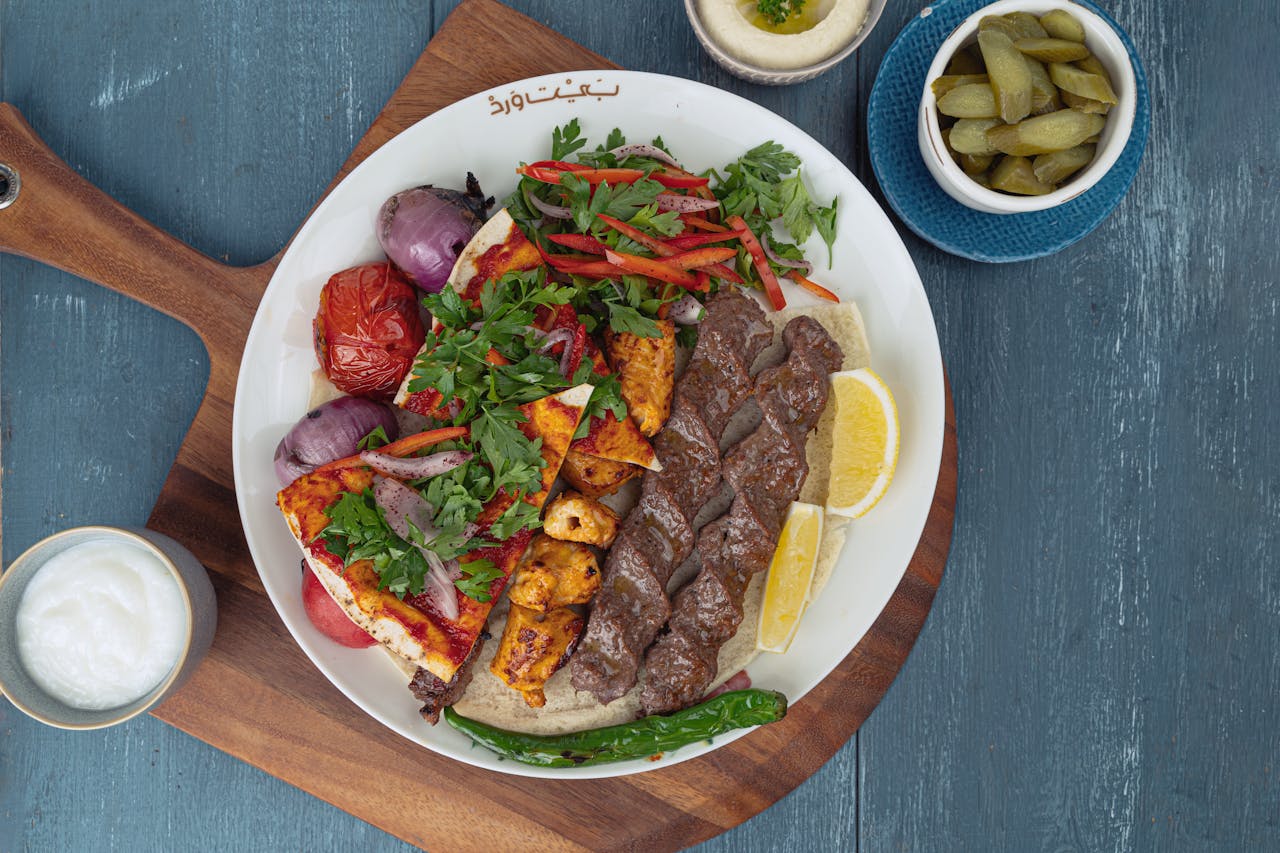 A colorful Middle Eastern mixed grill with kebabs, veggies, and sides on a serving board.